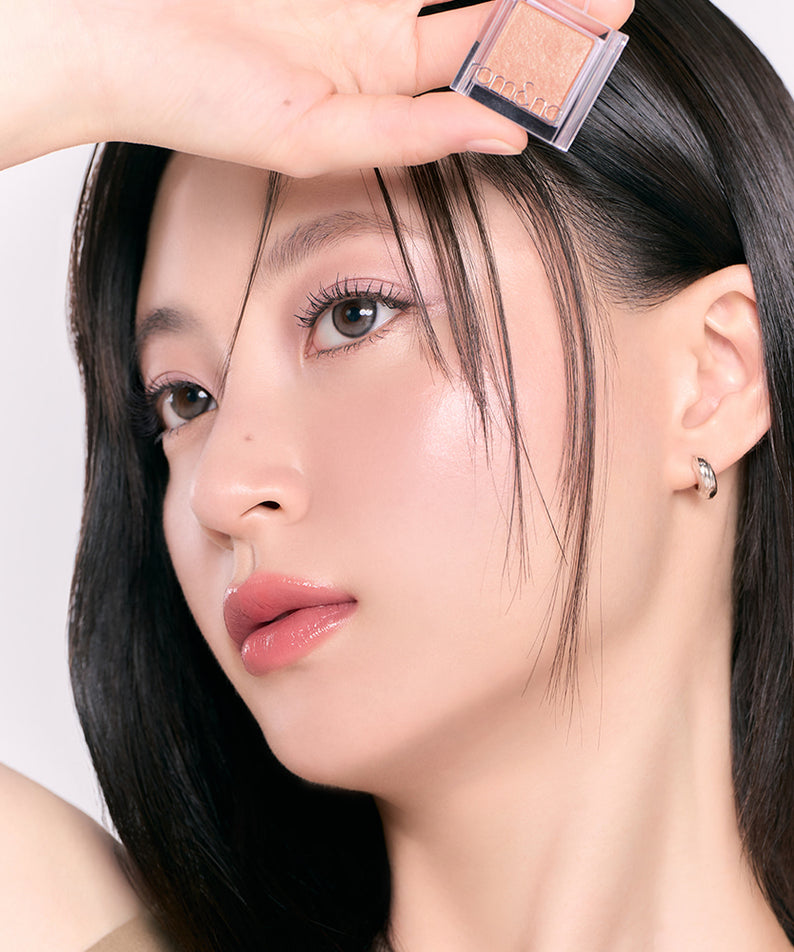 Femme posant avec le maquillage appliqué, mettant en valeur sa peau lisse et éclatante avec un produit de beauté, accentuant les yeux et les lèvres.