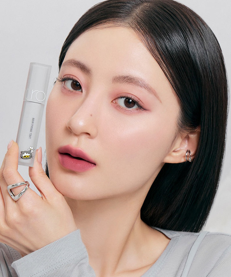 ROMAND x Joanne Friends Blur Fudge Tint, maquillage effet flou sur une femme aux cheveux noirs tenant le produit, fond clair.