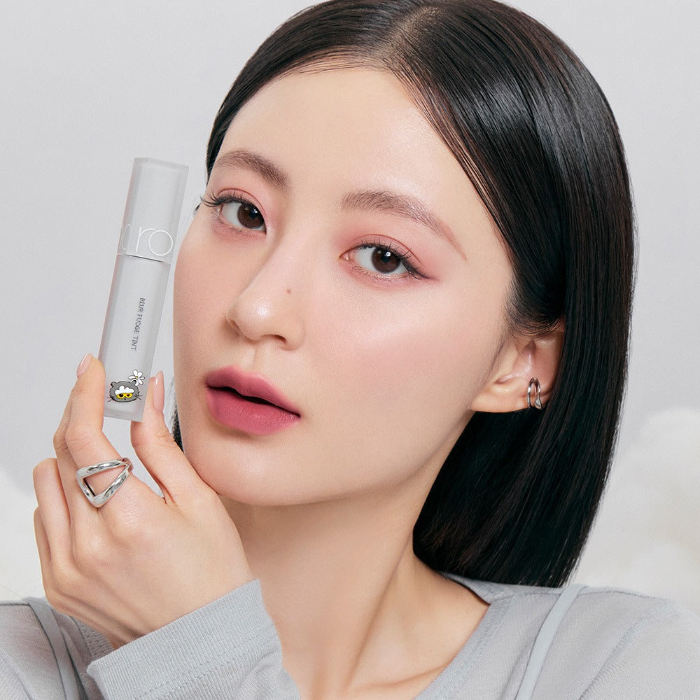 ROMAND x Joanne Friends Blur Fudge Tint, maquillage effet flou sur une femme aux cheveux noirs tenant le produit, fond clair.