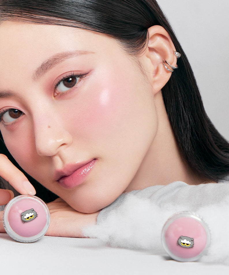 ROMAND x Joanne Friends Juicy R Cheek (Special Set) de ROMAND sur le visage d’une femme, avec poudres roses en décor.