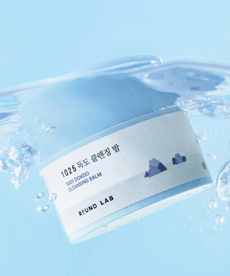 ROUND LAB 1025 Dokdo Cleansing Balm 50ml de ROUND LAB, posé dans des éclaboussures d’eau bleue.