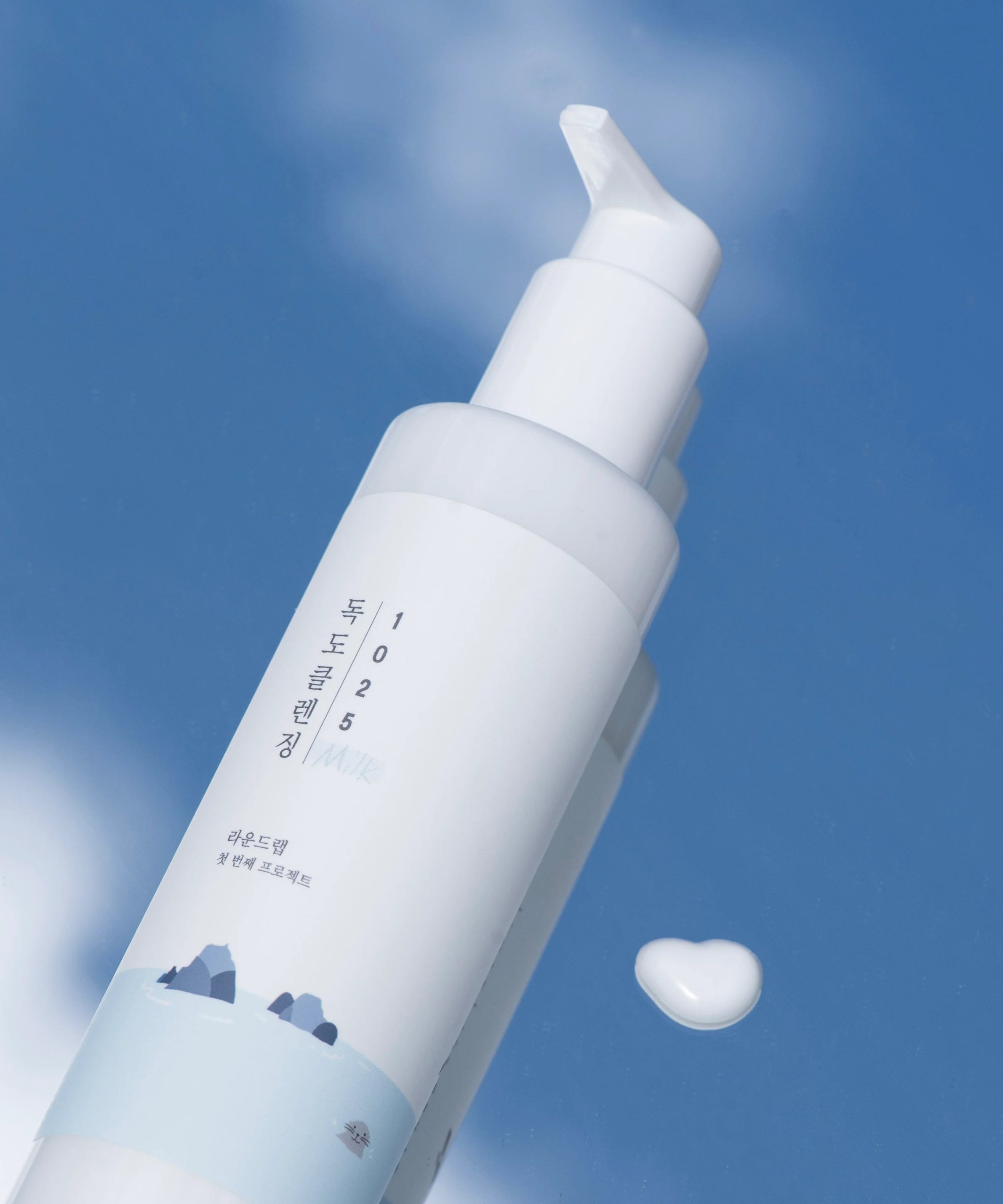 Flacon de ROUND LAB 1025 Dokdo Cleansing Milk 200ml avec texture crème blanche sur fond bleu ciel.
