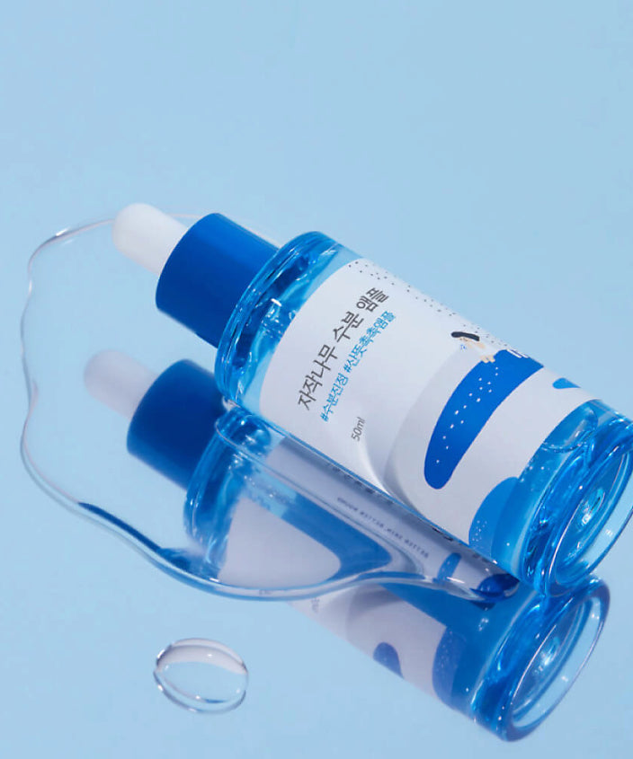 ROUND LAB Birch Moisture Ampoule 50ml posée sur une surface bleue, design moderne et éclat de douceur.