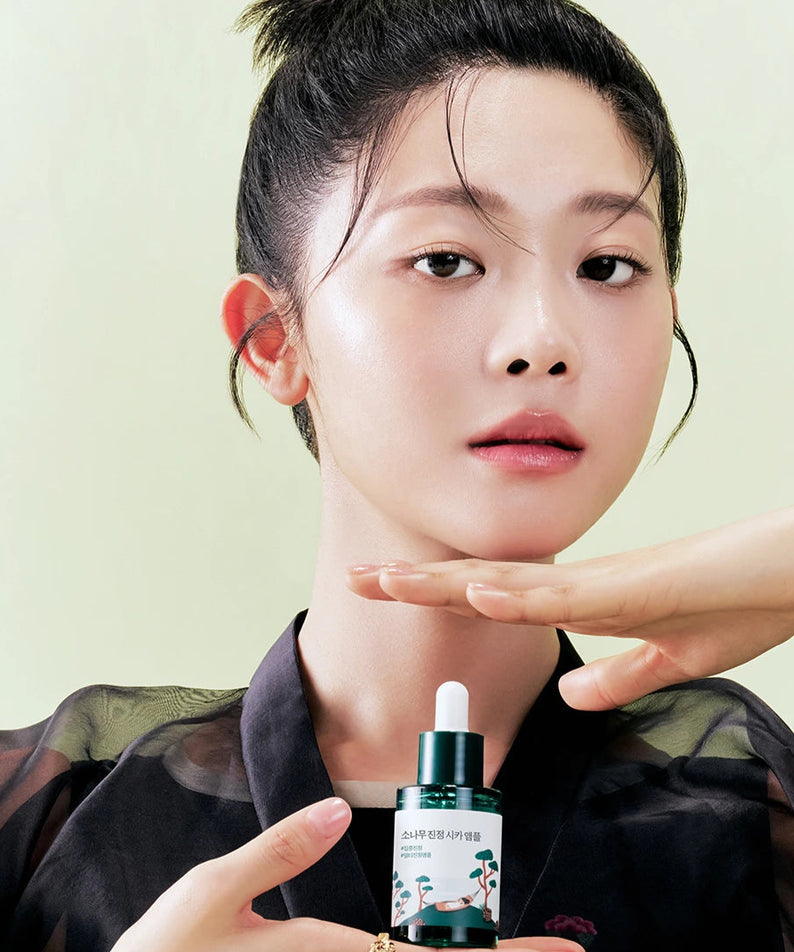 Femme tenant un flacon de ROUND LAB Pine Calming Cica Ampoule 30ml devant un fond clair.