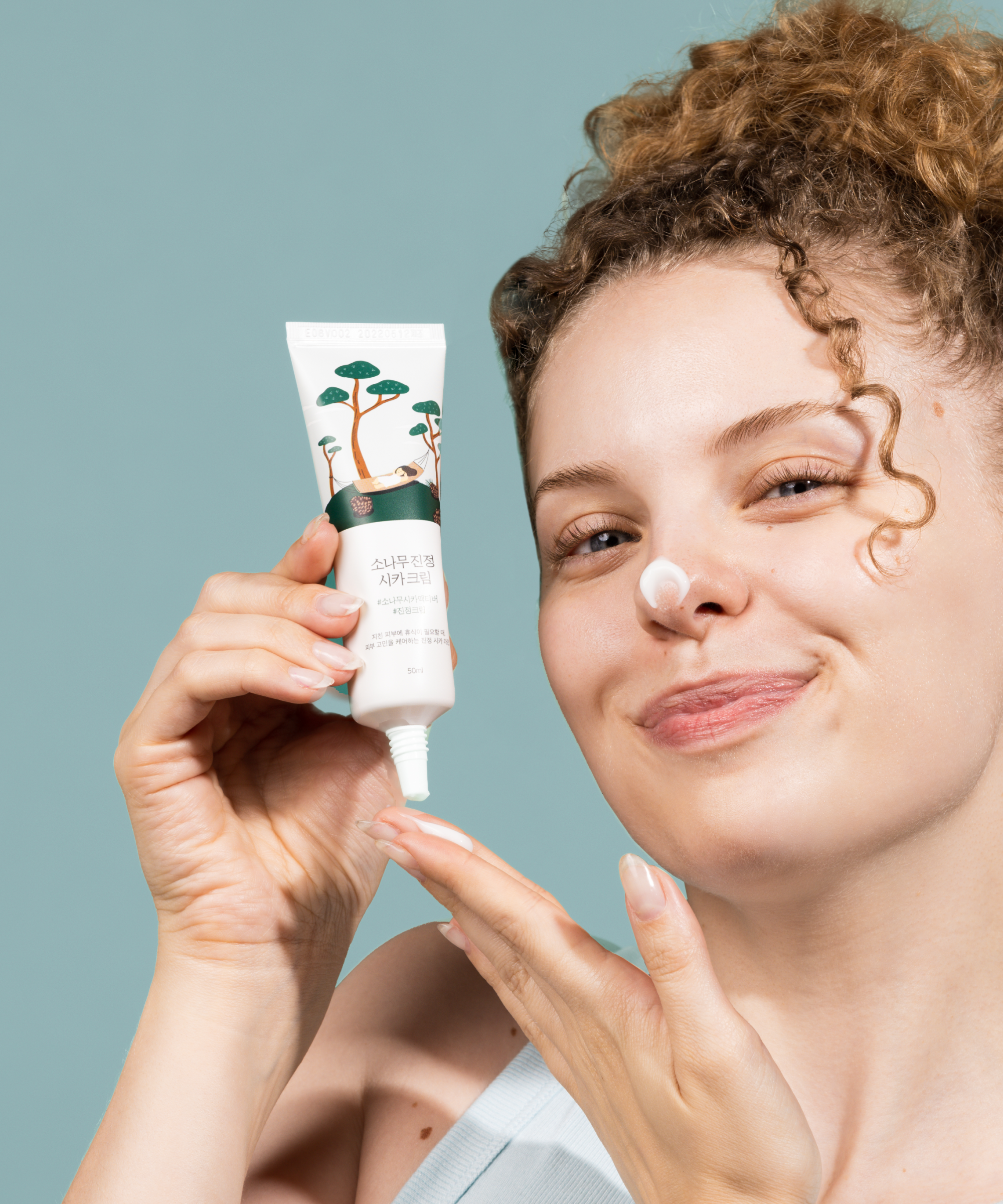 Femme souriante appliquant le ROUND LAB Pine Calming Cica Cream 50ml sur la peau, parfait pour apaiser et hydrater en douceur.