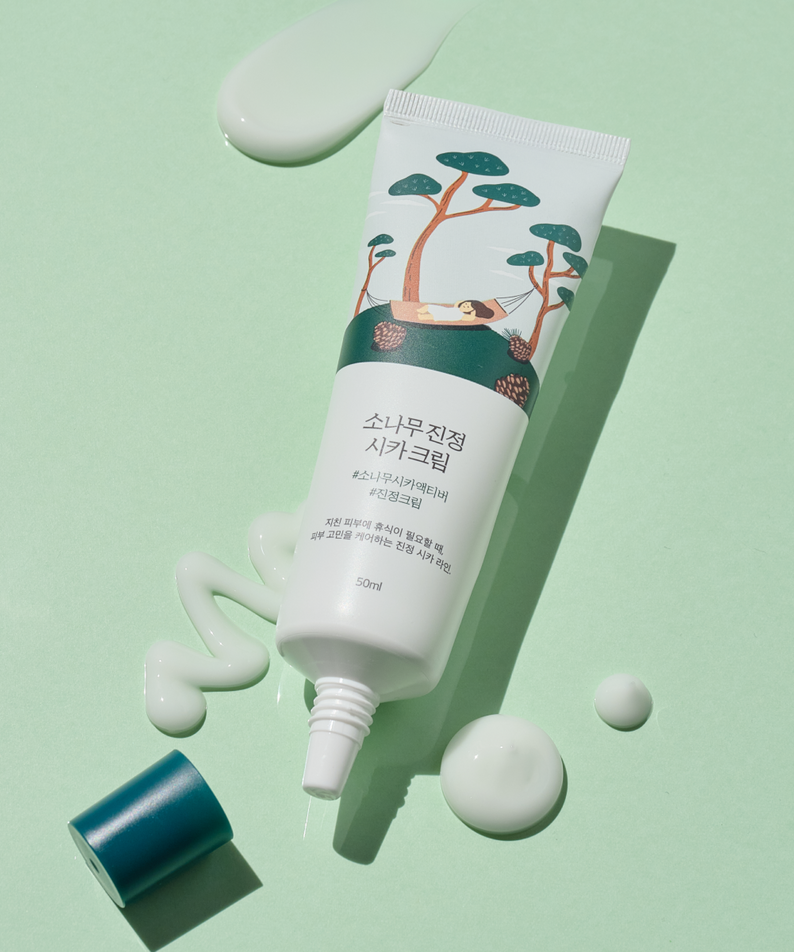 Crème apaisante ROUND LAB Pine Calming Cica Cream 50ml sur fond vert avec crème étalée, tube illustré de pins et bouchon bleu.