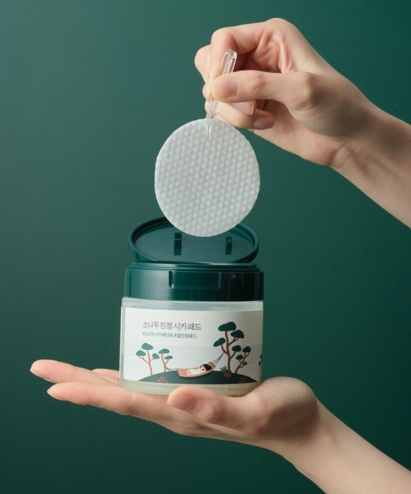 ROUND LAB Pine Calming Cica Pads 50 sheets : mains tenant un pad rond, produit ROUND LAB sur fond vert