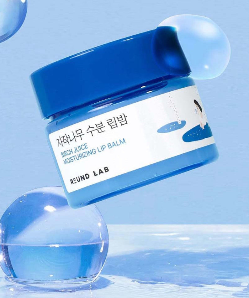 Baume à lèvres hydratant ROUND LAB Birch Moisture Lip Balm 20g, pot bleu flottant sur fond bleu avec gouttes d'eau.