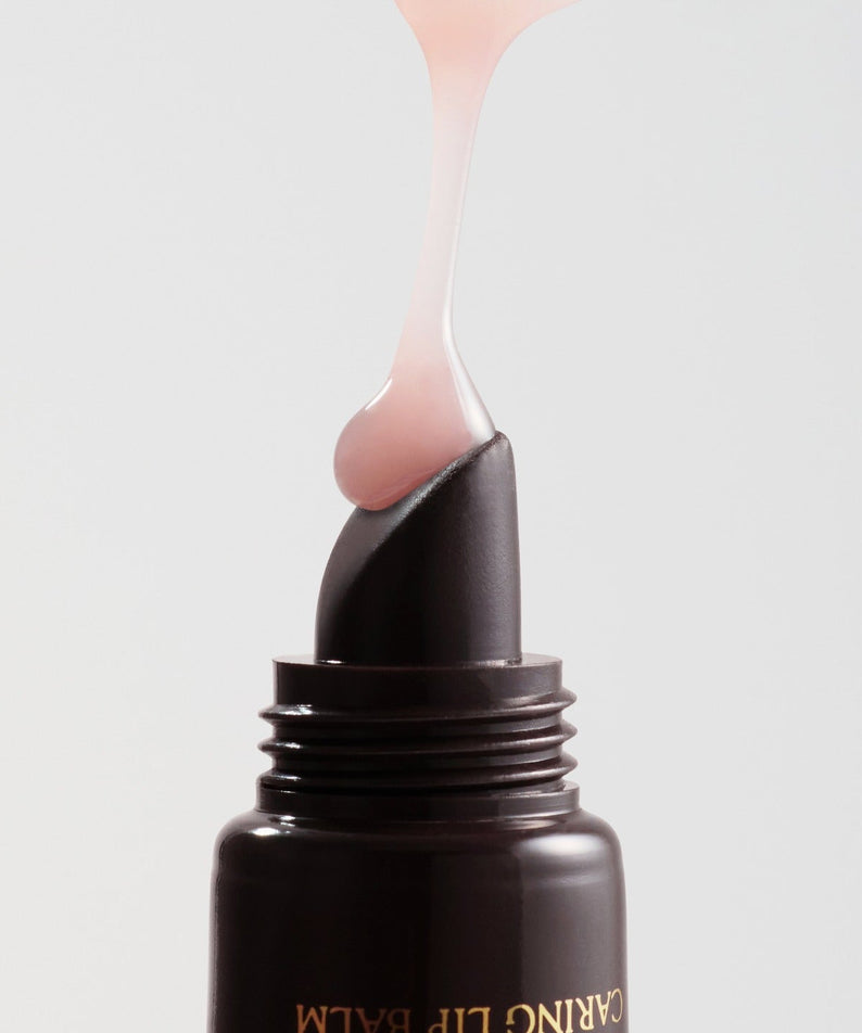 RULIDIA Shining Moment Caring Lip Balm 8g, baume lèvres appliqué en goutte sur flacon noir, fond clair.