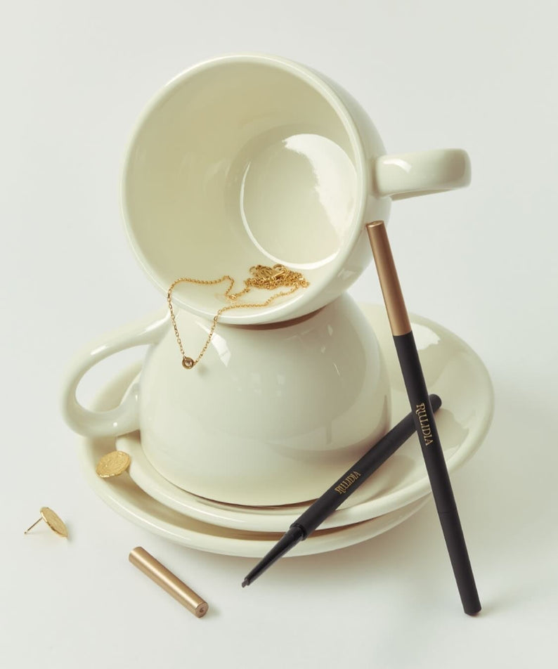 RULIDIA Easy Detail Brow disposé avec élégance à côté d'une tasse en céramique blanche, mettant en valeur un maquillage précis et raffiné.