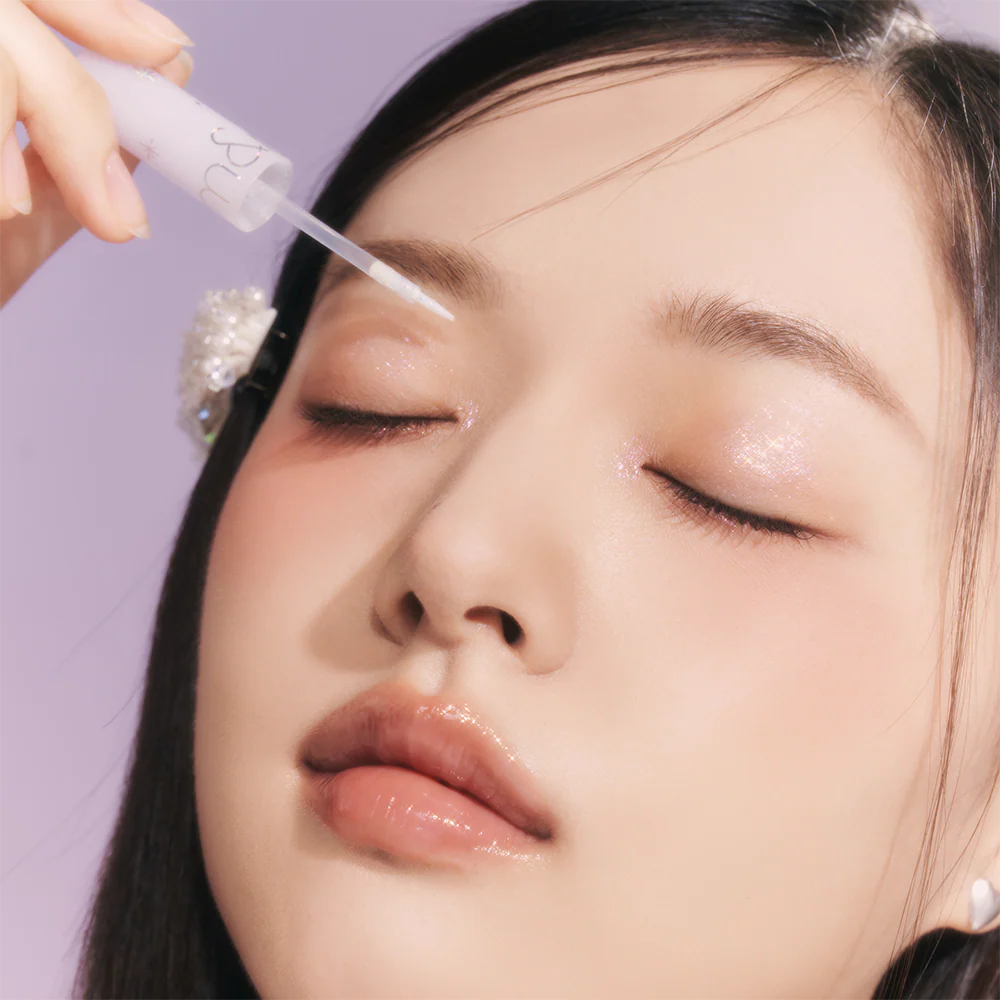 ROMAND The Universe Liquid Glitter, maquillage yeux pailletés sur visage, marque Romand en contexte violet, main appliquant