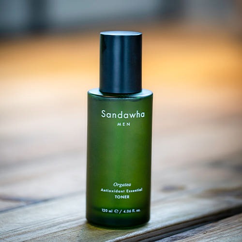 Décris l'image en français : SANDAWHA For Men orgatea Antioxidant Essential Toner 120ml, flacon vert sur table, flou arrière-plan.