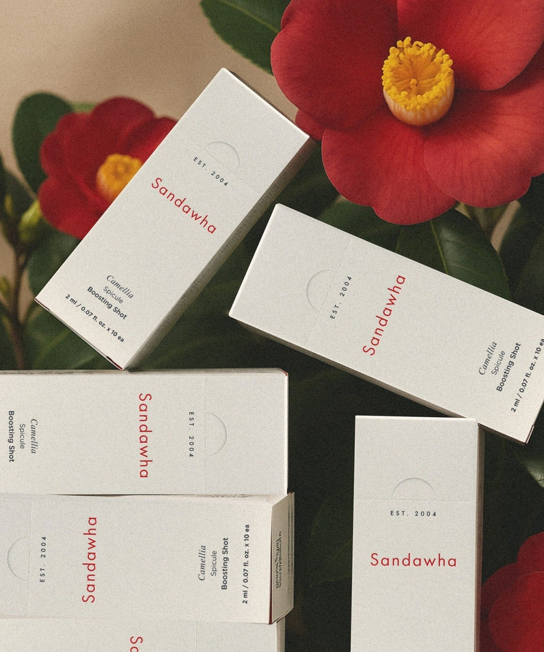 Boîtes de SANDAWHA Camellia Spicule Boosting Shot entourées de fleurs rouges.