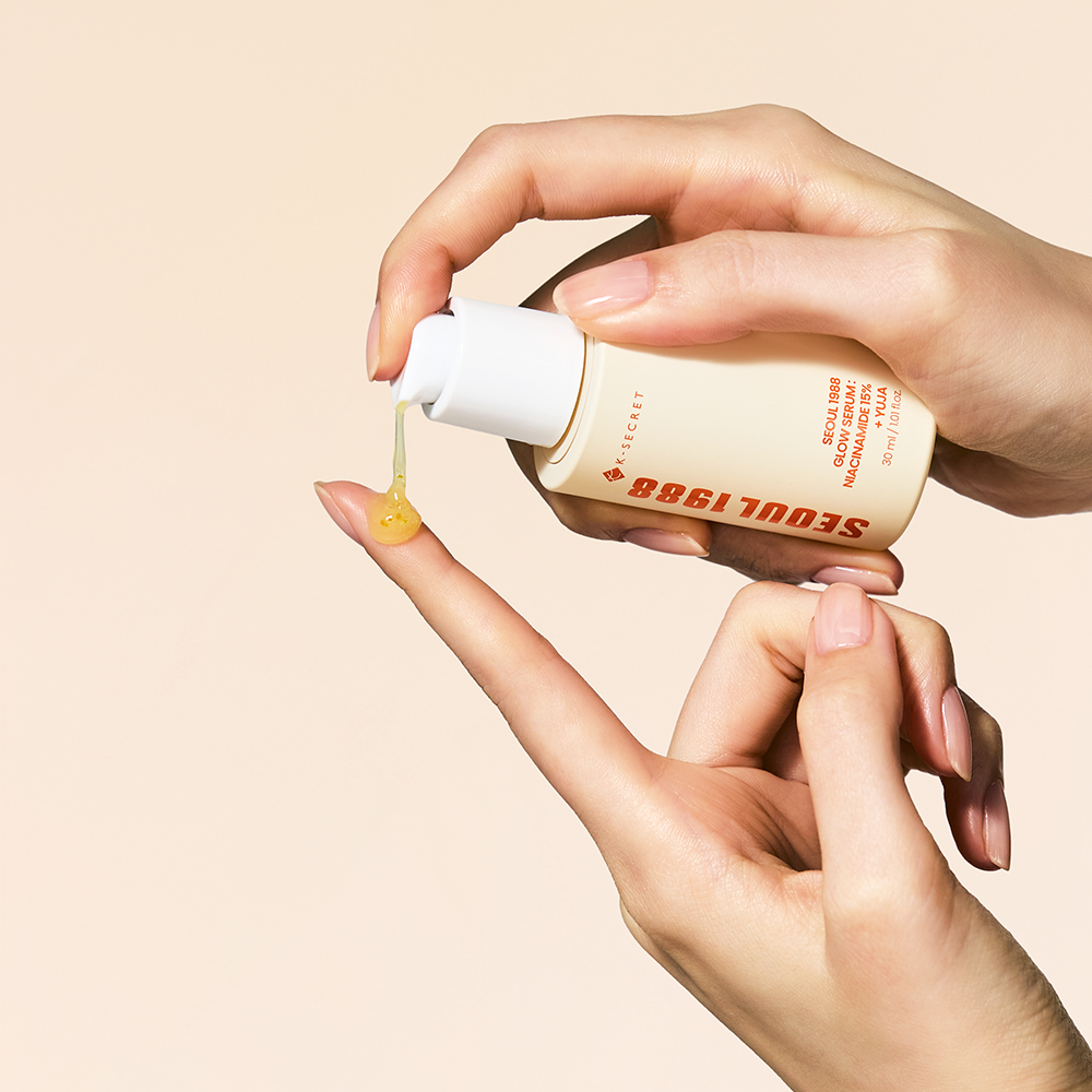 Main tenant SEOUL 1988  Niacin Yuja Serum 30ml, gouttes jaunes, fond beige, contexte skincare beauté.