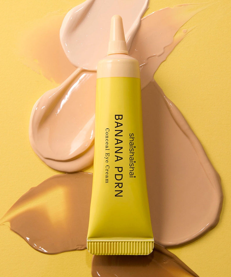 Décris l'image en français : SHAISHAISHAI Banana PDRN Conceal Eye Cream 15ml de la marque, tube sur fond jaune, texture crème.