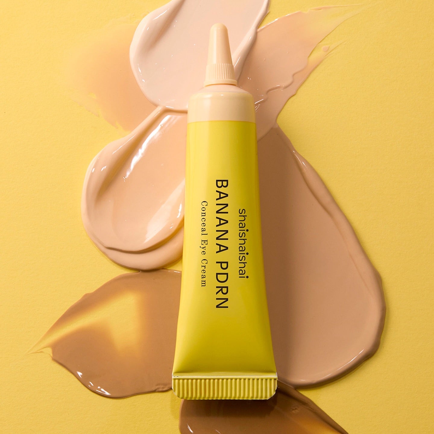 Décris l'image en français : SHAISHAISHAI Banana PDRN Conceal Eye Cream 15ml de la marque, tube sur fond jaune, texture crème.