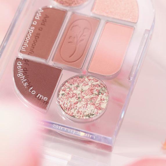 SIM;PLAIN Eye Palette de SIM;PLAIN, palette de fards roses et pailletés en boîte transparente sur fond maquillage