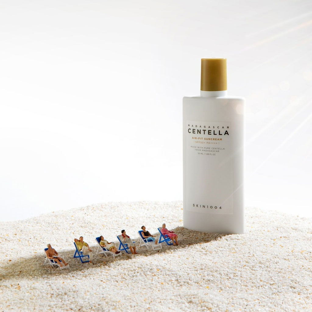 SKIN1004 Madagascar Centella Air-fit Sunscreen Plus 50ml, bouteille crème solaire sur sable blanc avec enfants au soleil.