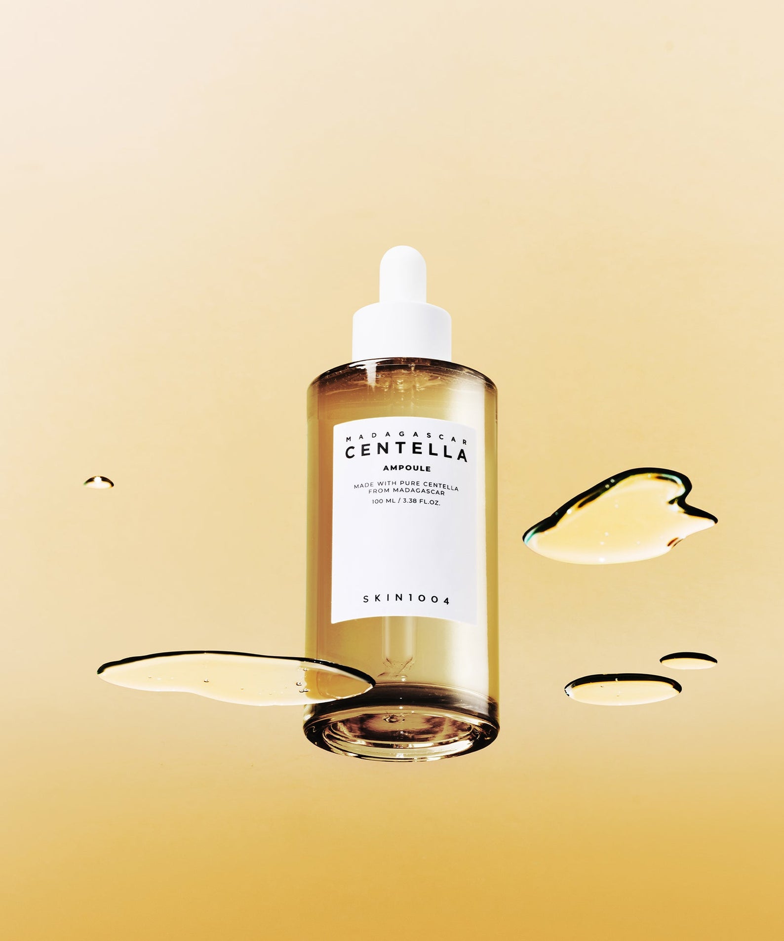 SKIN1004 Madagascar Centella Ampoule 100ml de SKIN1004 sur fond beige, gouttes de sérum illustrées, contexte visuel beauté.
