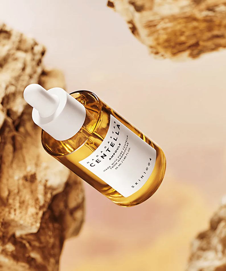 SKIN1004 Madagascar Centella Ampoule 55ml, flacon d’ampoule en verre ambre avec goutte blanche sur fond rocheux.