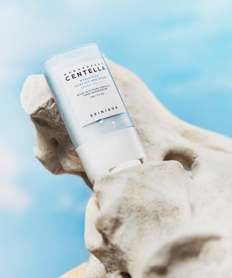 SKIN1004 Madagascar Centella Hyalu-Cica Silky Fit Sun Stick 20g de SKIN1004, sur fond bleu ciel avec ambiance resort.