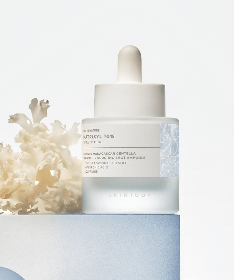 SKIN1004 Madagascar Centella Matrixyl 10 Boosting Shot Ampoule 30ml, flacon blanc sur fond clair avec fleurs en arrière-plan.