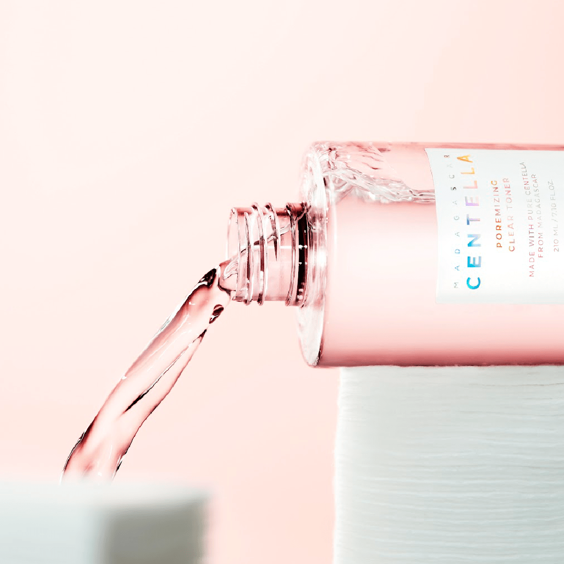 SKIN1004 Madagascar Centella Poremizing Clear Toner 210ml, flacon rose et mains vers le spray, contexte beauté.