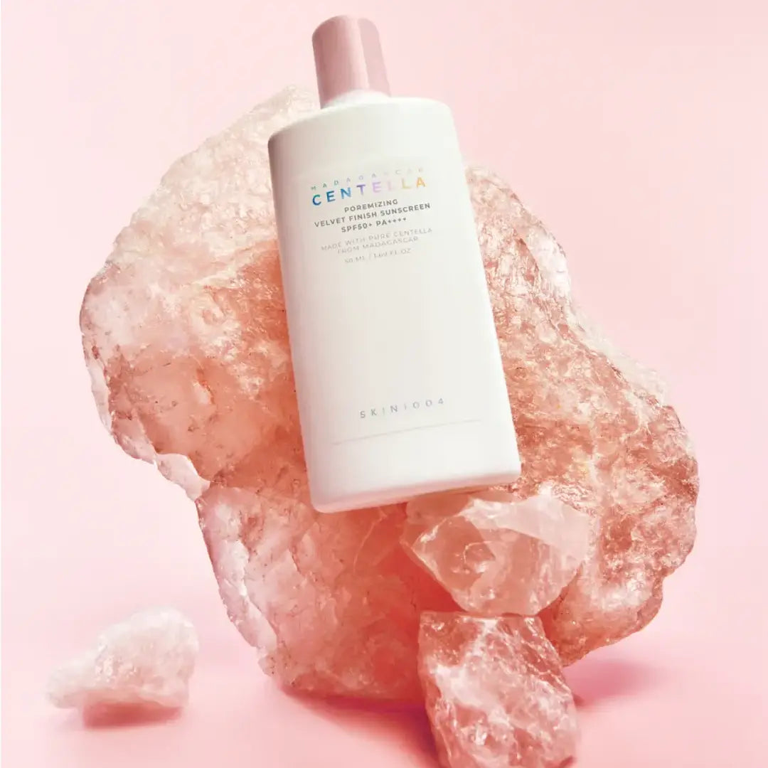 SKIN1004 Madagascar Centella Poremizing Velvet Finish Sunscreen 50ml, flacon crème, sur fond rose avec pierre minérale.