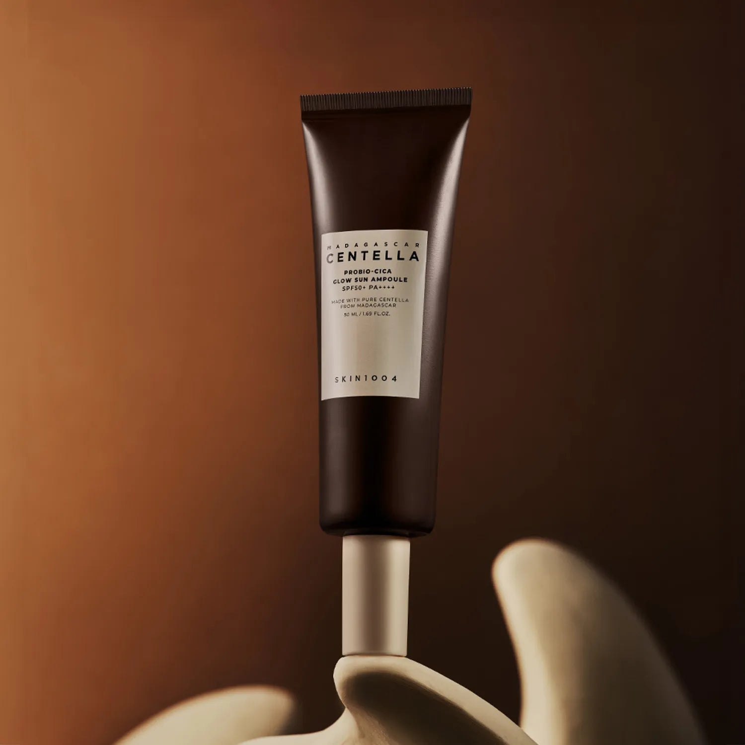 SKIN1004 Madagascar Centella Probio-cica Glow Sun Ampoule 50ml, tube crème sur fond brun avec ambiance beauté.