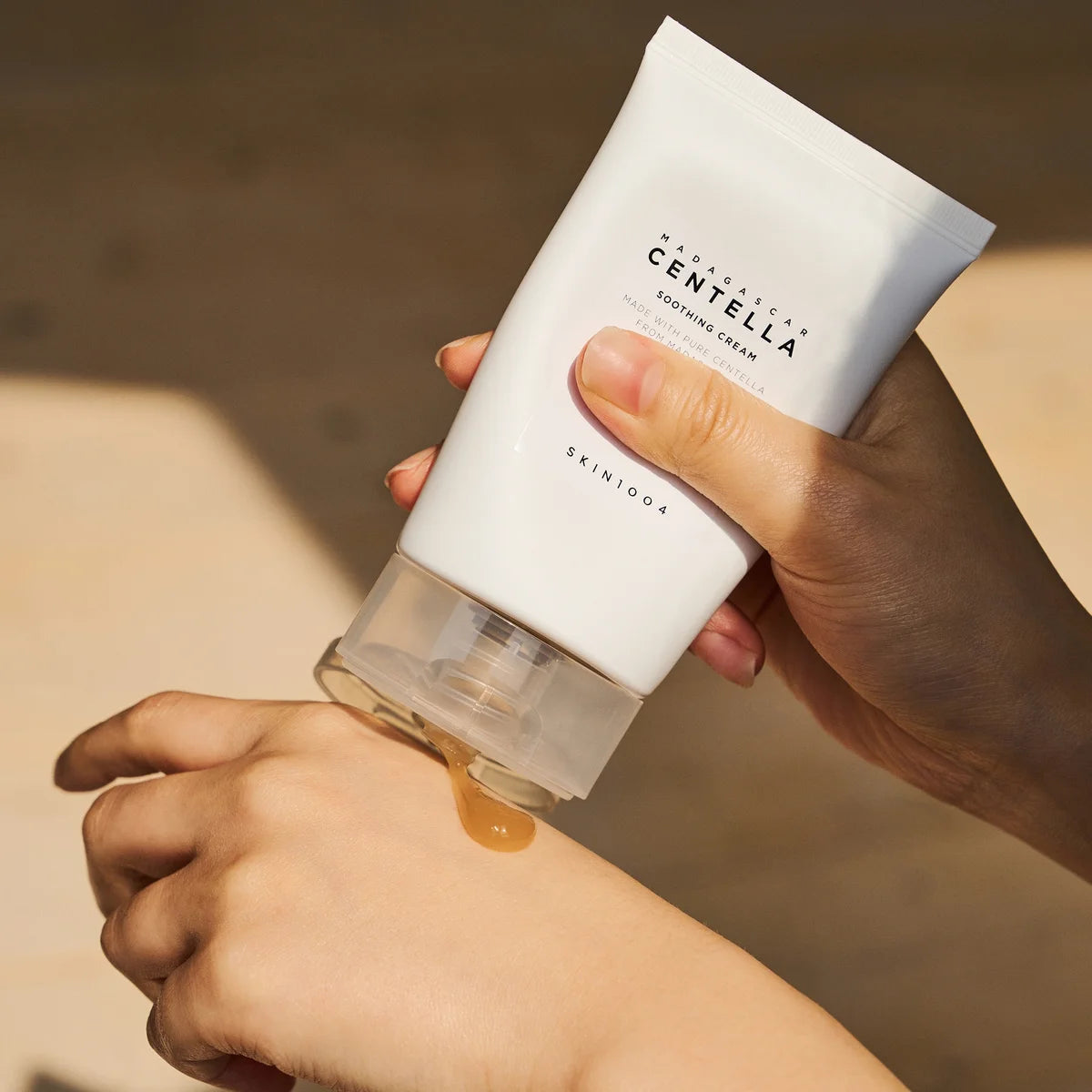 Main tenant SKIN1004 Madagascar Centella Soothing Cream 75ml de SKIN1004, crème apaisante sur fond beige, contexte beauté