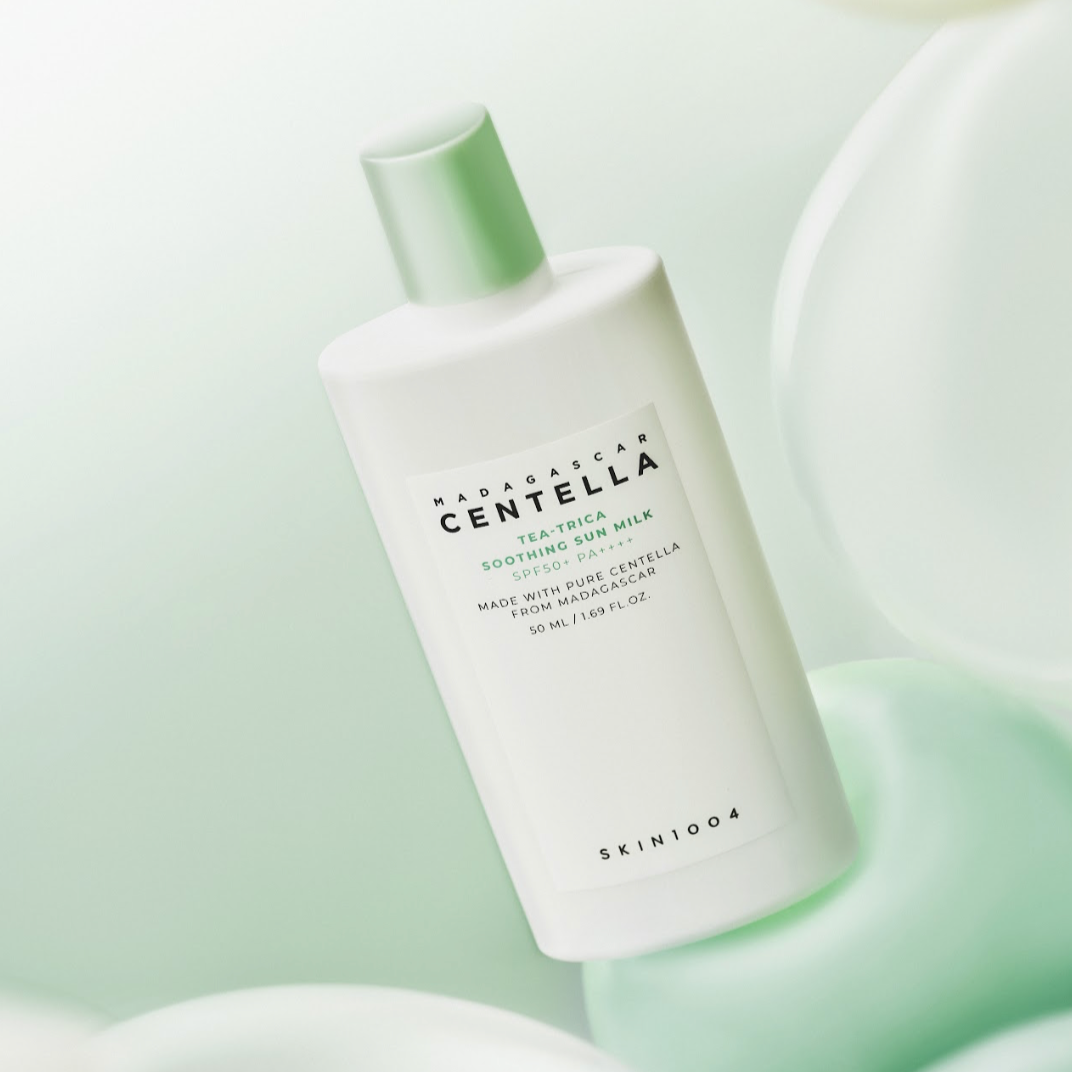 Décris l'image en français : SKIN1004 Madagascar Centella Tea-trica Soothing Sun Milk 50ml de SKIN1004, flacon blanc vert sur fond pastel.