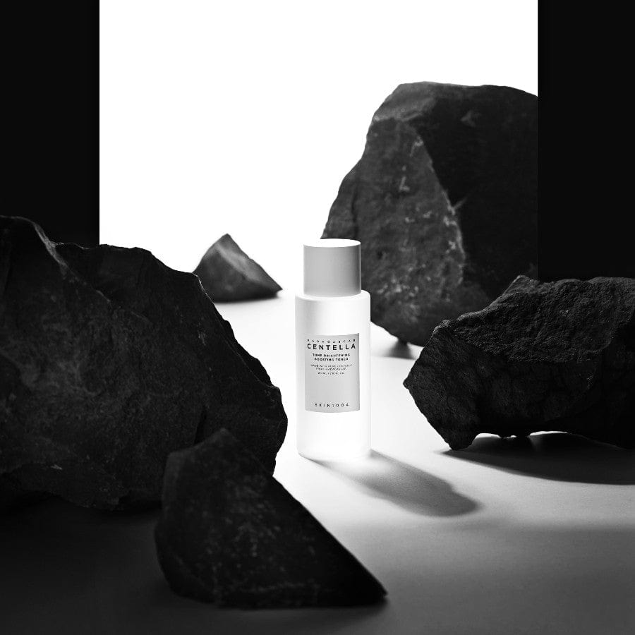 SKIN1004 Madagascar Centella Tone Brightening Boosting Toner 210ml en flacon blanc, marque SKIN1004, sur rochers noirs.