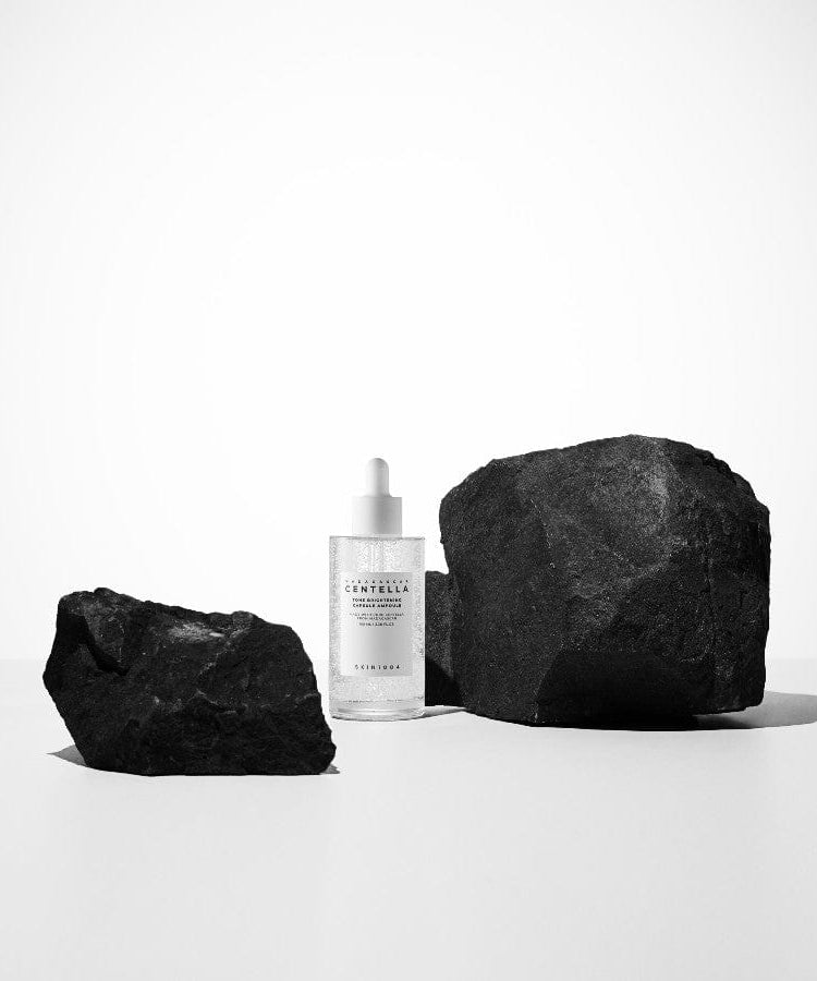 SKIN1004 Madagascar Centella Tone Brightening Capsule Ampoule 100ml, marque SKIN1004, flacon blanc sur pierres noires, studio blanc.