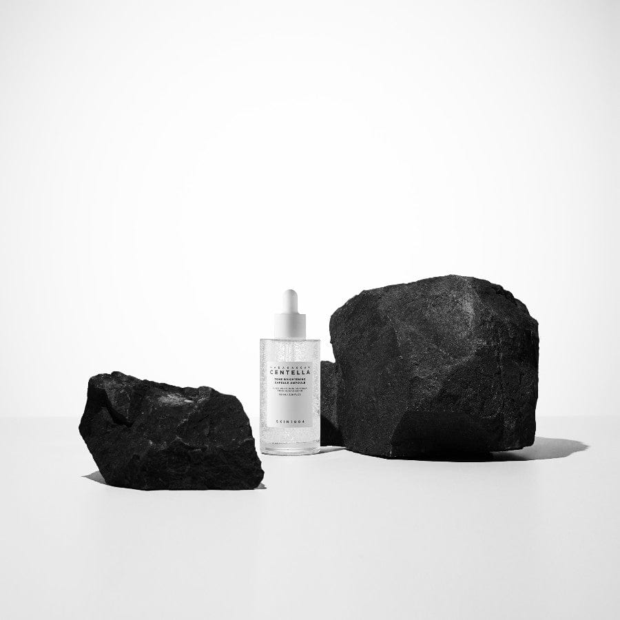 SKIN1004 Madagascar Centella Tone Brightening Capsule Ampoule 100ml, marque SKIN1004, flacon blanc sur pierres noires, studio blanc.