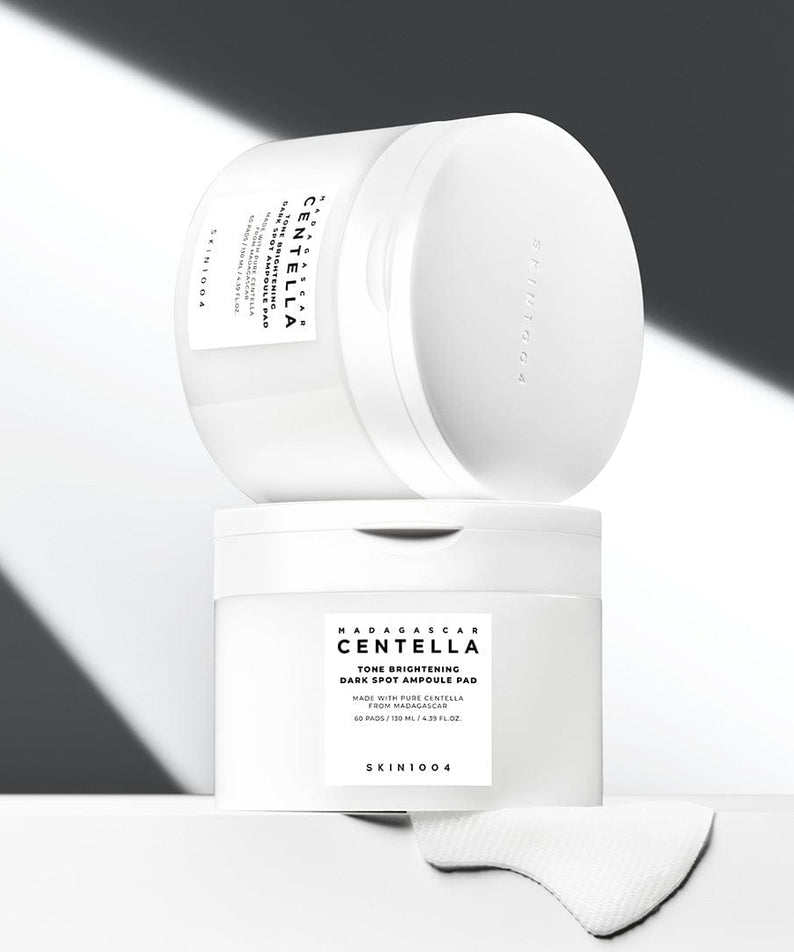 SKIN1004 Madagascar Centella Tone Brightening Dark Spot Ampoule Pads (60 sheets) de SKIN1004 sur fond minimaliste blanc/gris, gants et boîte
