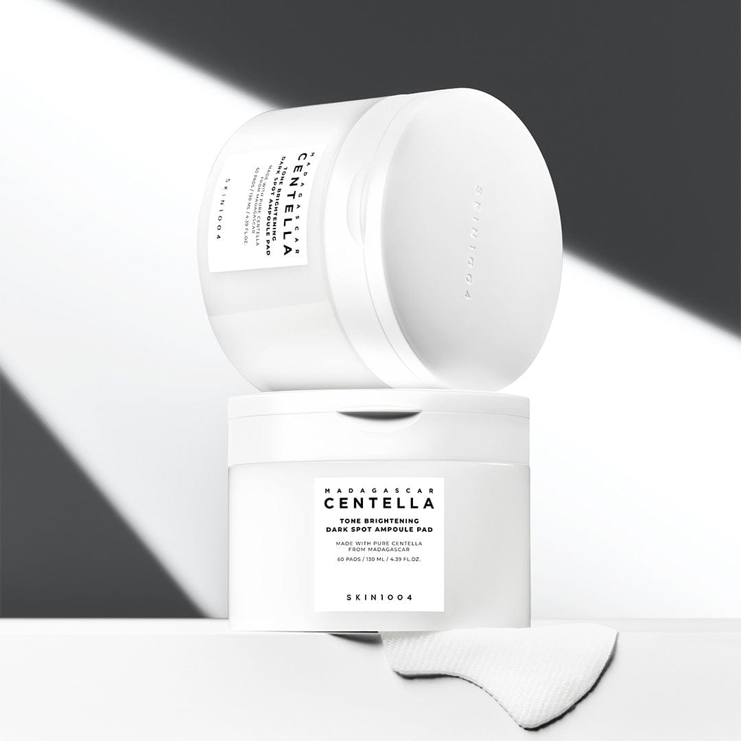 SKIN1004 Madagascar Centella Tone Brightening Dark Spot Ampoule Pads (60 sheets) de SKIN1004 sur fond minimaliste blanc/gris, gants et boîte