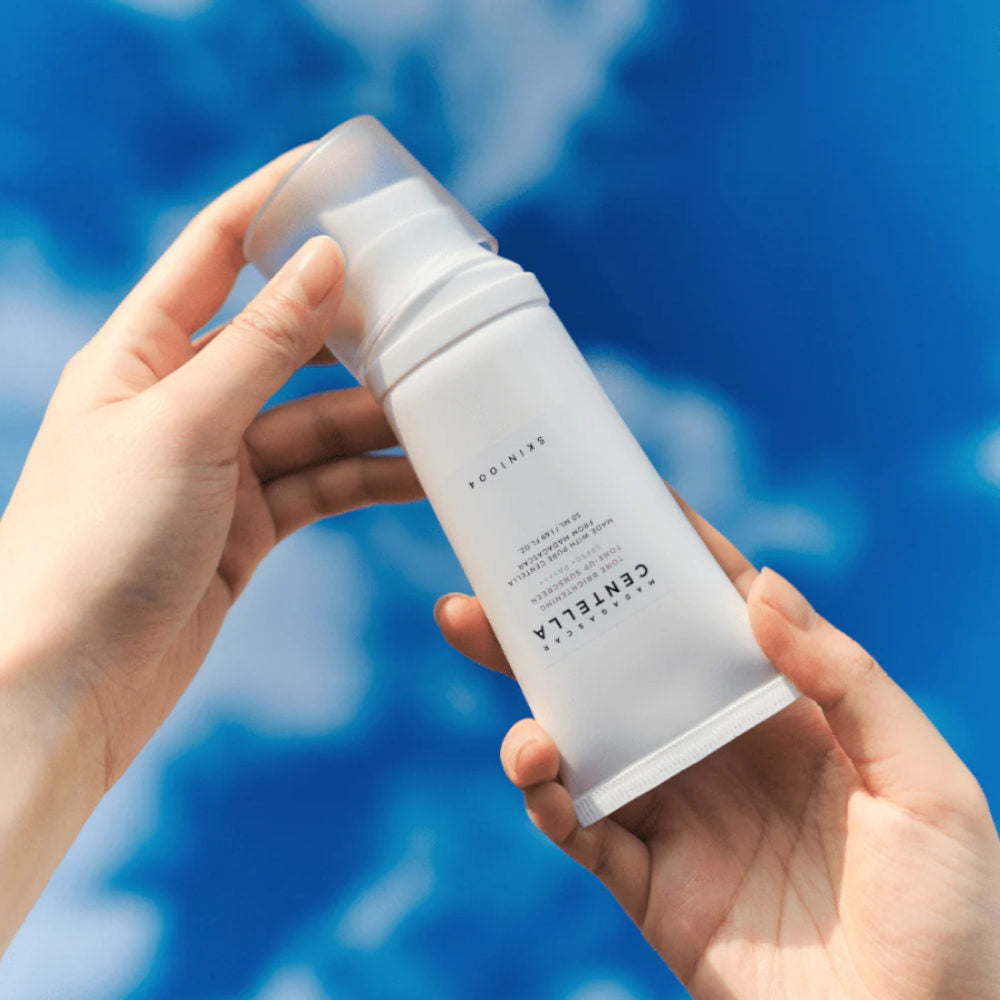 SKIN1004 Madagascar Centella Tone Brightening Tone-Up Sunscreen 50ml de la marque SKIN1004, tube tenu sur fond bleu.