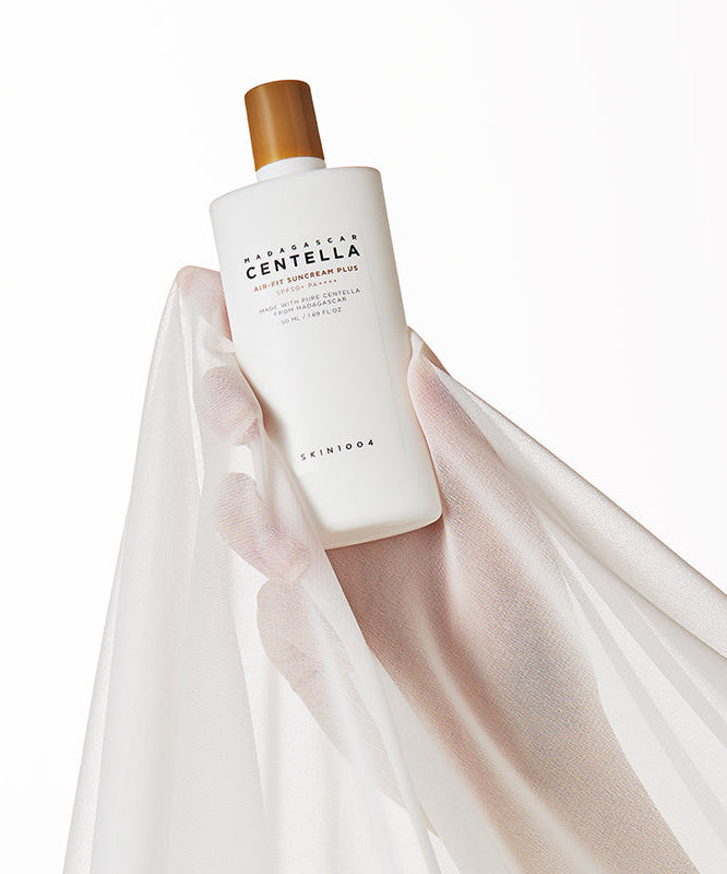 SKIN1004 Madagascar Centella Air-fit Sunscreen Plus 50ml en main avec un voile blanc subtil en arrière-plan, accentuant son élégance.
