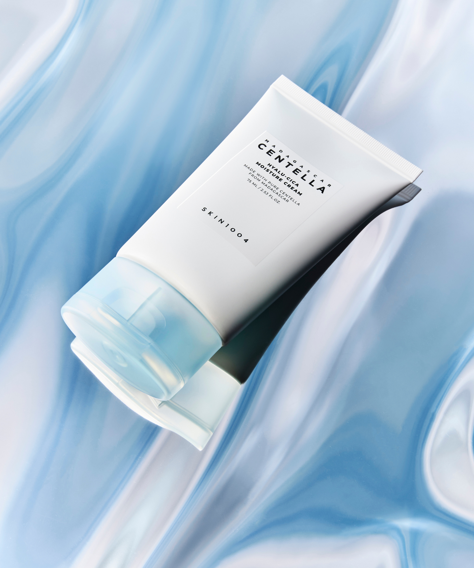 Crème hydratante SKIN1004 Madagascar Centella Hyalu-Cica Moisture Cream 75ml posée sur un fond bleu aquatique.