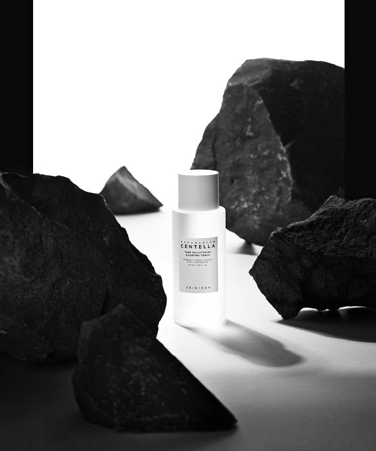 SKIN1004 Madagascar Centella Tone Brightening Boosting Toner 210ml entourée de roches noires, en arrière-plan dramatique.