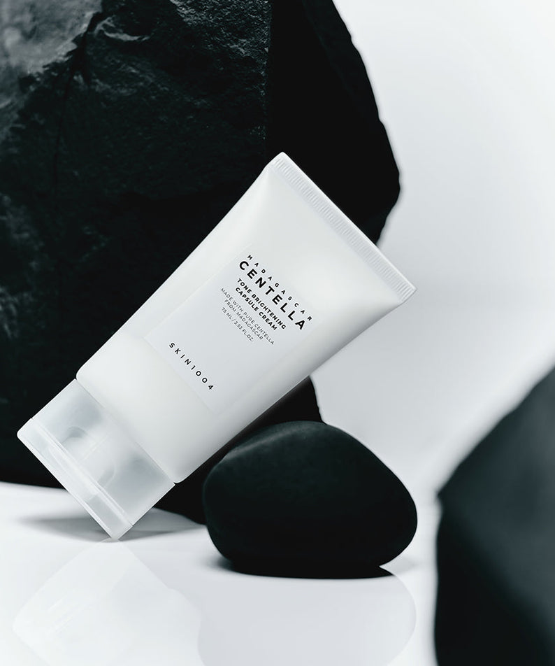 Crème SKIN1004 Madagascar Centella Tone Brightening Capsule 75ml posée sur des roches noires, fond minimaliste moderne.