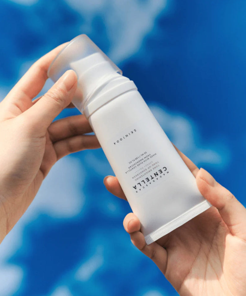 SKIN1004 Madagascar Centella Tone Brightening Tone-Up Sunscreen 50ml tenu dans une main sous un ciel bleu.