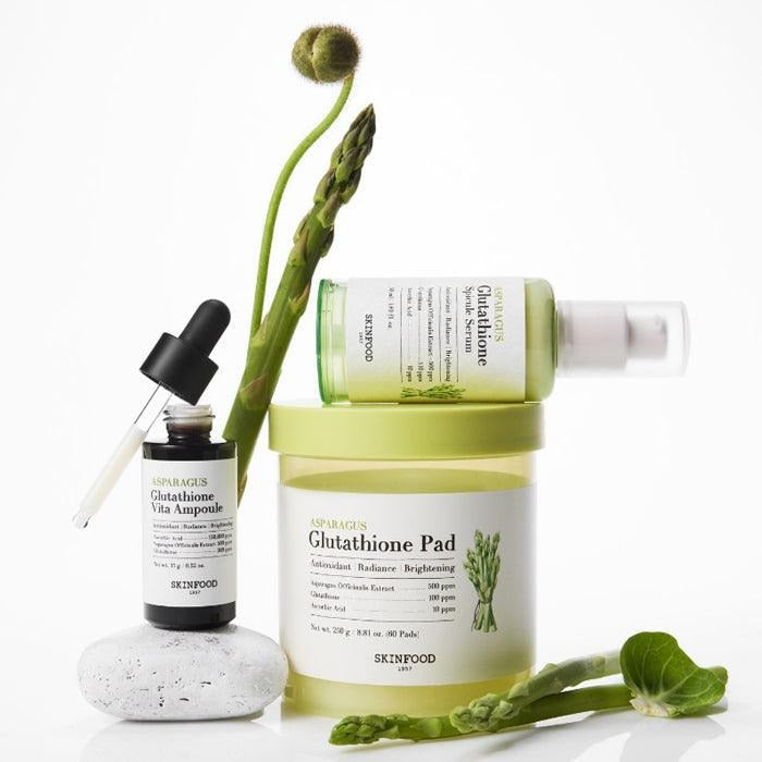 SKINFOOD Asparagus Glutathione Pad (60 Pads) de SKINFOOD, flacons et sérum sur fond blanc, tiges d’asperge.