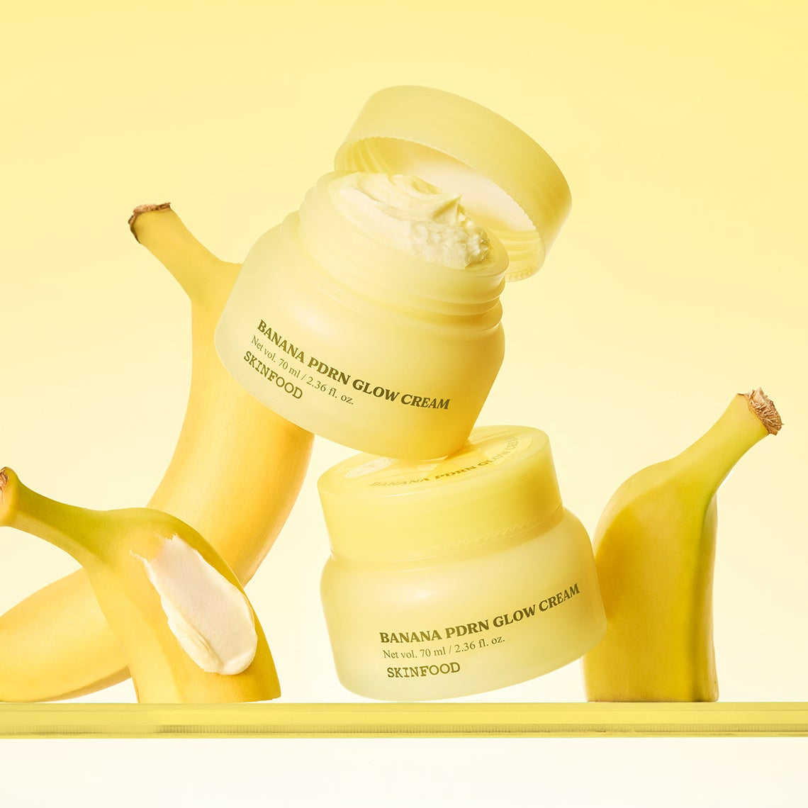 SKINFOOD Banana PDRN Glow Cream 70ml de marque SKINFOOD, crème lumineuse avec bananes, fond jaune en studio.
