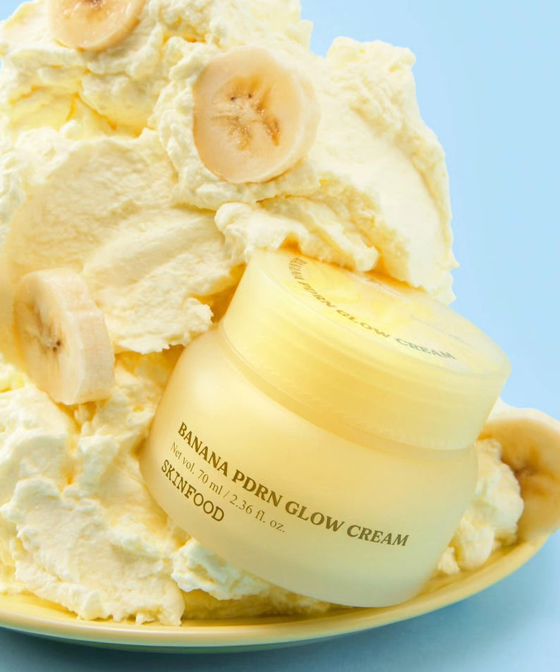SKINFOOD Banana PDRN Glow Cream 70ml, crème lissante sur fond bleu avec banane et texture crémeuse, photo produit.