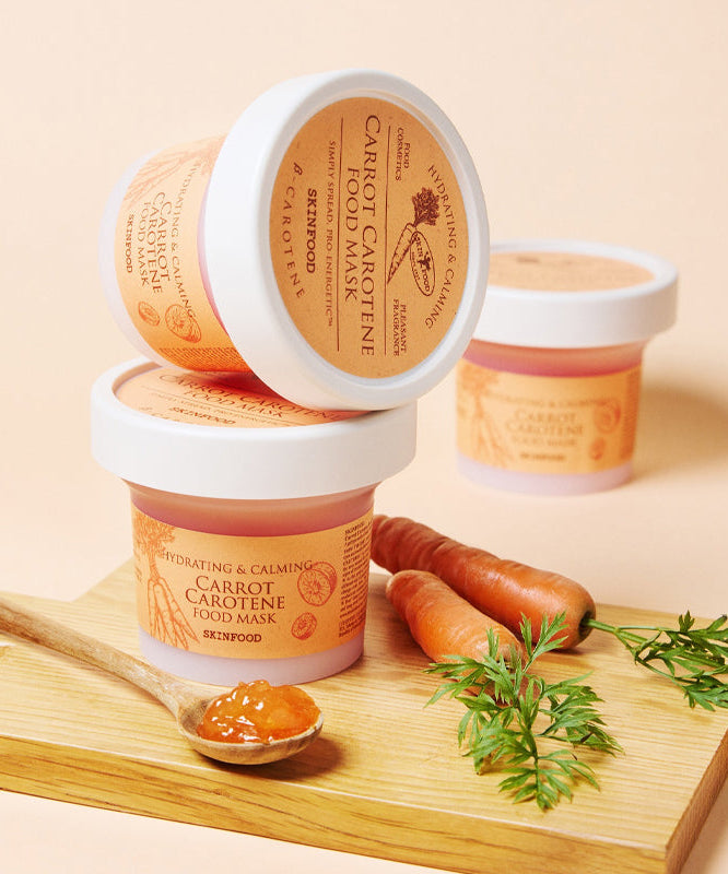 SKINFOOD [NEW ] Carrot Food Mask 120g de la marque SKINFOOD, pots sur planche bois, carottes et herbes, fond beige.
