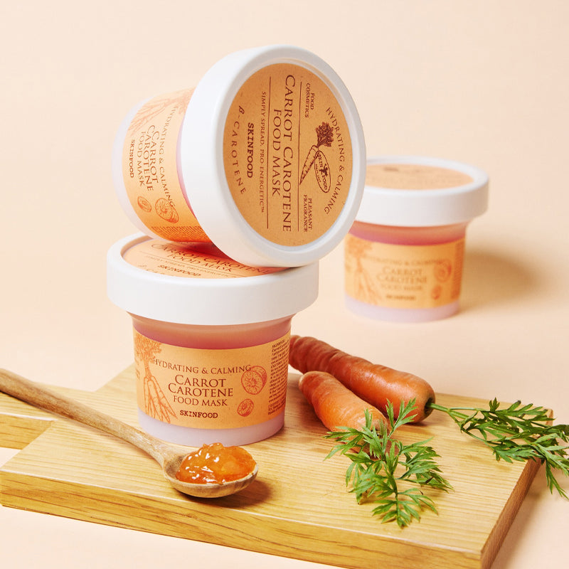SKINFOOD [NEW ] Carrot Food Mask 120g de la marque SKINFOOD, pots sur planche bois, carottes et herbes, fond beige.