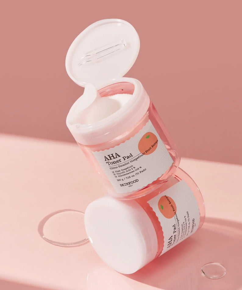 SKINFOOD Pink Grapefruit AHA Toner Pad 70 sheets, pads et flacon ouverts sur fond rose, packshot produit marque SKINFOOD