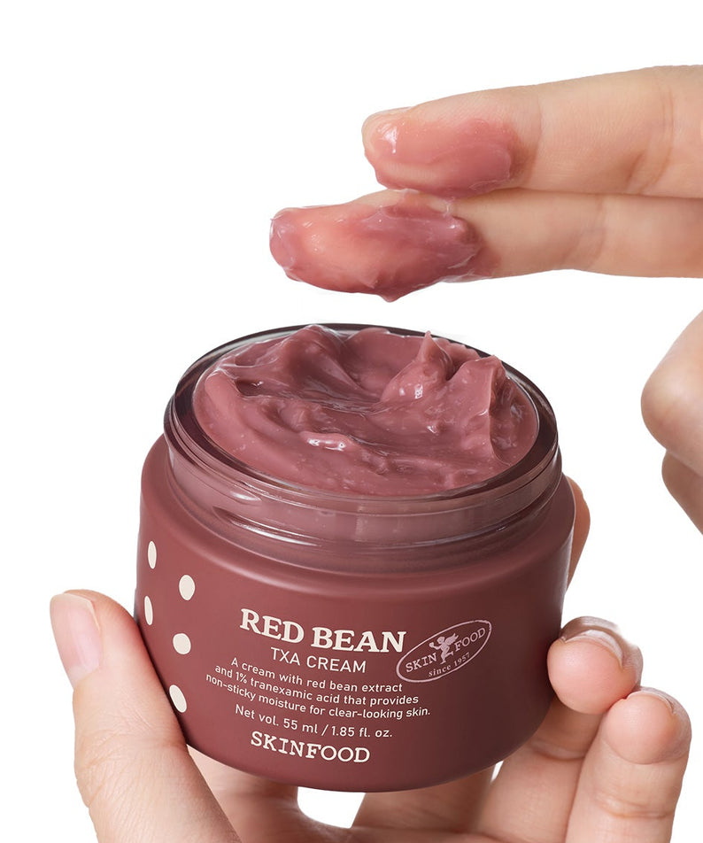 SKINFOOD Red Bean Tranexamic Acid Cream 55ml en pot brun, texture crème rose, main tenant le produit sur fond blanc.