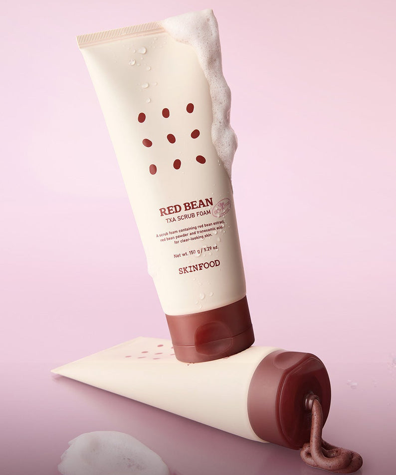 Décris l'image en français : SKINFOOD Red Bean Tranexamic Acid Scrub Foam 150g, tube et mousse sur fond rose.
